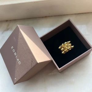 Guldfärgad ring från Edblad - Snygg guldfärgad ring från Edblad med ett unikt designmönster av små pyramidformade detaljer. Perfekt för att ge en edgy touch till din stil. Kommer i originalförpackning.