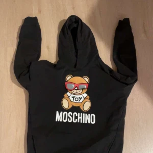 Moschino hoodie - Säljer en svart hoodie från Moschino med ett coolt nalletryck på framsidan. Hoodien har långa ärmar och en klassisk huva. Perfekt för en avslappnad stil med en touch av lekfullhet.