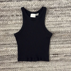 Svart ribbad linnetopp från Gina Tricot - Säljer en stilren svart ribbad linnetopp från Gina Tricot. Toppen har en enkel design med rund hals och ärmlös stil, perfekt för en avslappnad. 🖤