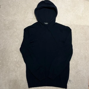 Mörkblå stickad hoodie - Säljer en stilren mörkblå stickad hoodie med långa ärmar och justerbar huva. Den är väldigt snygg och liknar de populära kashmir och merino tröjorna. Denna är 50% ull och 50% bomull. Vid minsta fråga eller fundering hör av er🤝