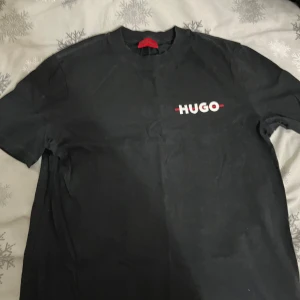 Svart t-shirt från Hugo - Snygg svart t-shirt från Hugo med vit logga på bröstet. Perfekt för en stilren look. Kortärmad och i mjukt material för bekväm passform. Pris kan diskuteras!!
