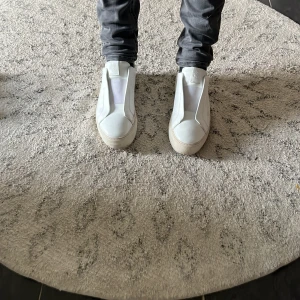 Vita sneakers från Axel Arigato - Snygga vita sneakers från Axel Arigato med en stilren design. Skorna har en slät yta utan snörning och en diskret logotyp på sidan. Perfekta för en minimalistisk look.