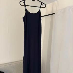 Mörkblå långklänning med smala axelband - Elegant mörkblå långklänning med smala justerbara axelband. Perfekt för en stilren och minimalistisk look. Klänningen är använd 1 gång. Storlek L men sitter som M