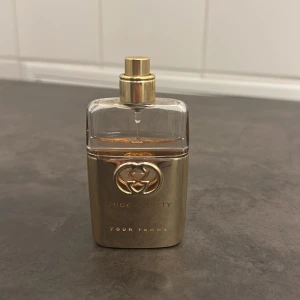 Gucci Guilty Pour Femme parfym - Elegant parfymflaska från Gucci Guilty Pour Femme i en lyxig guld- och glasdesign. Flaskan har en stilren form med det ikoniska Gucci-emblemet på framsidan. Perfekt för den som vill ha en sofistikerad doftupplevelse.