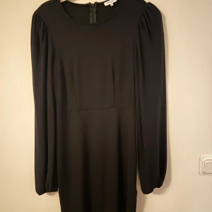 Svart klänning från Bubbleroom - Elegant svart klänning från Bubbleroom med långa ärmar och rund hals. Perfekt för en stilren look. Klänningen har en enkel design som gör den lätt att matcha med olika accessoarer.