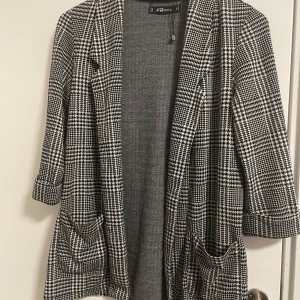 Rutig kavaj från FB Sister - Snygg rutig kavaj från FB Sister i svart och vitt. Kavajen har trekvartsärmar och två fickor framtill. Perfekt för en stilren look.