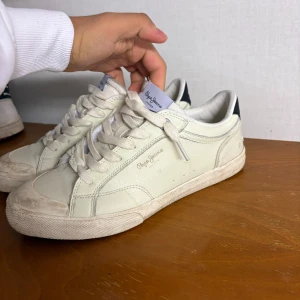 Vita sneakers från Pepe Jeans - Snygga vita sneakers från Pepe Jeans med snörning och svart detalj med '1973' på hälen. Perfekta för en avslappnad stil. Tillverkade i syntetmaterial med en klassisk design. Kan tvättas så dom blir helt nya använt dom fåtal gånger 