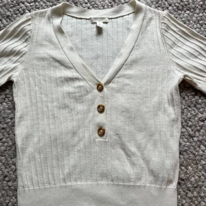 Vit ribbad topp från H&M - Säljer en vit ribbad topp från H&M med v-ringning och tre knappar. Toppen är sparsamt använd och väldigt fin!