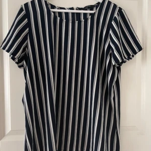 Randig kortärmad blus från Vero Moda  - Snygg blus med vertikala ränder i svart och vitt. Den har korta ärmar och en rund halsringning. Perfekt för en stilren look.