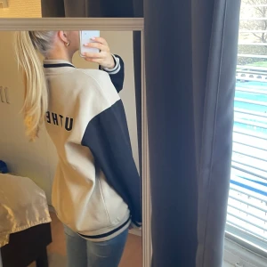Beige och svart varsity jacka - Säljer en snygg beige varsityjacka med svarta ärmar och detaljer. Jackan har knappar framtill och en klassisk bomberstil. Den är knappt använd och i väldigt bra skick. Den är i storlek XS men är oversized och passar mig som bär storlek S.