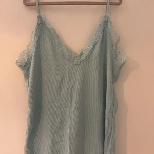 Ljusgrön/ljusblå ribbat linne med spetsdetaljer - Säljer ett gulligt ljusgrön/ljusblå ribbat linne med v-ringad spetskant, använd max en gång så i jätte bra skick🩵