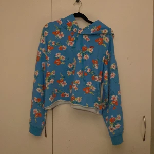 Blommig blå hoodie från Levi's - Säljer en färgglad blå hoodie från Levi's med ett blommigt mönster i rosa, orange och vitt. Hoodien har långa ärmar och en bekväm passform. Perfekt för att liva upp garderoben! 🌸
