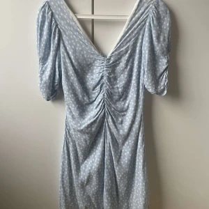 Ljusblå prickig klänning från Zara - Säljer en söt ljusblå klänning från Zara med vita prickar. Klänningen har en v-ringad design och korta ärmar med rynkdetaljer. Perfekt för en somrig look! 🌸