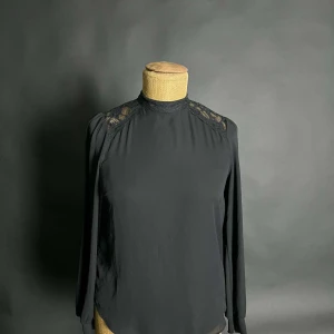 Svart blus med spetsdetaljer - Elegant svart blus med långa ärmar och vackra spetsdetaljer vid axlarna och övre ryggen. Perfekt för en stilren look.
