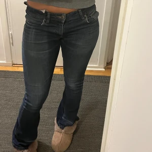 Blå bootcut jeans - Snygga blå bootcut jeans med låg midja. Perfekta för en avslappnad stil. Klassisk design med fem fickor och knappgylf.