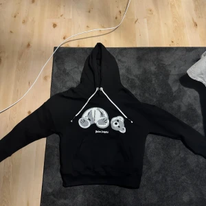 Svart hoodie  - Säljer en svart hoodie från med en unik nallebjörnsdesign på framsidan. Hoodien har en justerbar dragsko i huvan och en stor ficka framtill. Perfekt för en avslappnad stil.