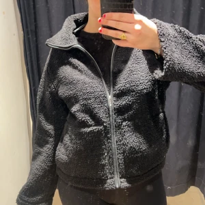 Svart teddyjacka med dragkedja - Mysig svart teddyjacka med dragkedja framtill. Perfekt för kyligare dagar med sin fluffiga och varma design. Jackan har en hög krage och långa ärmar, vilket gör den extra bekväm och stilren. Den är från lager 157 och sålde slut direkt! Endast använd en gång 🤗
