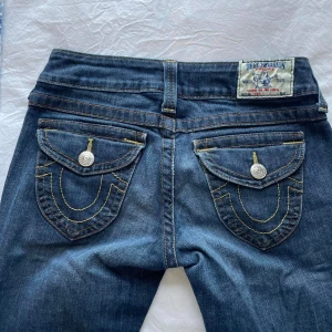 True religion bootcut - Snygga blå jeans från True Religion med ikoniska bakfickor och kontrastsömmar. De har en klassisk femficksdesign och knappgylf. Perfekta för en avslappnad stil.