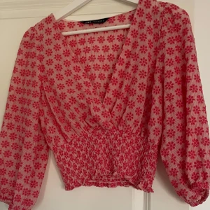 Rosa blommig blus från Zara - Säljer en söt blus från Zara i rosa med blommigt mönster. Blusen har en omlott-design och trekvartsärmar. Den är elastisk i midjan för en bekväm passform.
