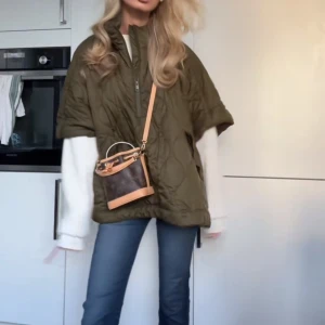 Olivgrön quiltad poncho - Säljer en olivgrön quiltad poncho med dragkedja framtill. Den har en loose passform och är perfekt för höst och vår. Ponchon har en hög krage och knappdetaljer vid sidorna för extra stil.💓