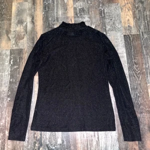 Svart glittrig tröja från Lindex, Holly & White - Svart, glittrig polotröja från Lindex, Holly & White. Tröjan har långa ärmar och en liten polokrage. Använt ganska mycket. Om du har frågor eller vill ha mer bilder kontakta mig🩷