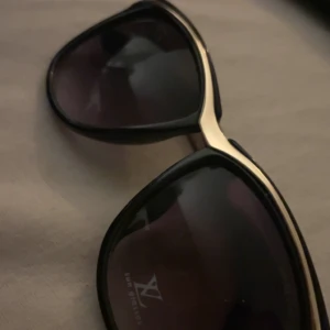 Svarta solglasögon med gulddetaljer - Snygga svarta solglasögon med eleganta gulddetaljer på bågarna. Perfekt för en stilren look med en touch av lyx. 