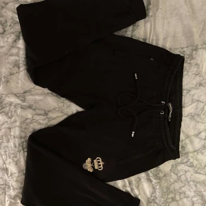 Svarta mjukisbyxor med broderi - Snygga svarta mjukisbyxor med broderad detalj på benet. De har en elastisk midja med snörning och muddar vid bensluten. Perfekta för en avslappnad stil.