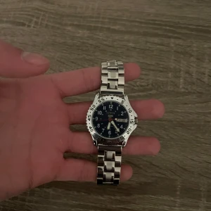 Autentisk Vintage Seiko 5 - Otroligt stilig och sällsynt Seiko 5 DayDate. Seiko loggan och dagarvisaren har guldplaterade detaljer, som matchar det automatiska och precisa klockuret med en open back case som ni kan se på andra bilden. Klockan är i otroligt bra skick som ni kan se. Säljer fler stiliga klockor och kläder på vår profil. Vid frågor eller funderingar skriv pm. Allt gott, mvh