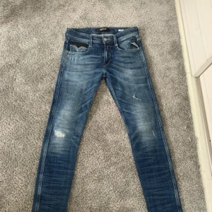 Blå jeans från Replay - Snygga blå jeans från Replay i modellen Anbass. De har en klassisk femficksdesign med dragkedja och knapp. Jeansen har en lätt slitning för en cool look och är perfekta för en avslappnad stil.