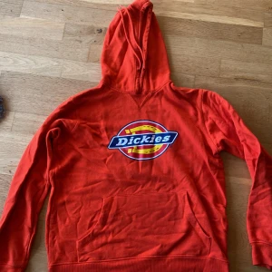 Orange hoodie från Dickies - Säljer en cool orange hoodie från Dickies med deras ikoniska logga på bröstet. Tröjan har en klassisk känguruficka och en bekväm huva. Perfekt för en avslappnad stil.
