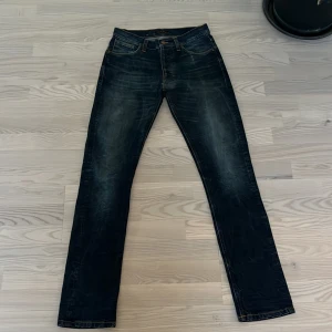 Nudie Jeans  - Snygga mörkblå jeans från Nudie Jeans med klassisk femficksdesign och orange sömmar. Jeansen har en straight passform och är perfekta för en avslappnad stil. Mer info eller bilder hör av er!