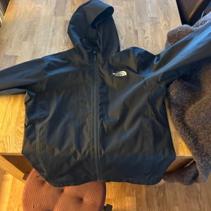 Svart vindjacka från The North Face - Säljer en svart vindjacka från The North Face. Jackan har en praktisk huva och dragkedja framtill. Perfekt för blåsiga dagar och enkel att matcha med olika outfits. hör av er om ni har frågor