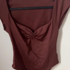 Brun/ vinröd bodysuit från Zara - Den är Ny jag köpte den i December men har aldrig kommit till användning. Säljer en snygg brun bodysuit från Zara. Den har en elegant v-ringning med rynkdetalj framtill och är ärmlös. Perfekt för att styla med olika outfits. Strl S men jag skulle säga att den även är Xs.