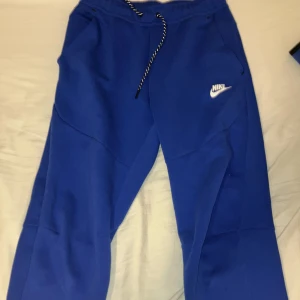 Nike tech mörkblå - Säljer en blå hoodie och matchande byxor från Nike. Hoodien har dragkedja och stort Nike-tryck på framsidan. Byxorna har snörning i midjan och fickor men har en fet fläck på vänstra armen