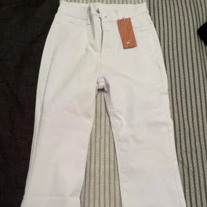 Vita jeansbyxor - Snygga vita jeansbyxor med hög midja och bootcut-stil. Byxorna har en dragkedja framtill och klassiska bakfickor. Perfekta för en stilren look.