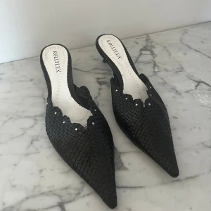 Svarta klackskor från Kollflex - Eleganta svarta klackskor från Kollflex med spetsig tå och flätat mönster. Skorna har en låg klack och dekorativa detaljer längs kanten. Perfekta för en stilren look.