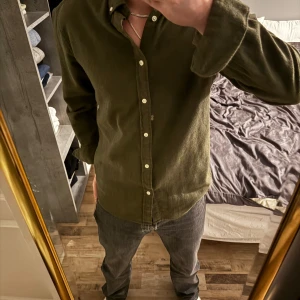 Grön flanell skjorta - Snygg olivgrön flanell skjorta med klassiska knappar. Skjortan har långa ärmar och en normal passform, perfekt för en stilren look. Passar bra till både jeans och chinos.