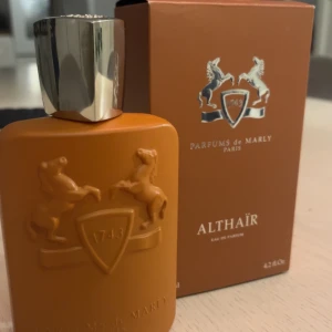 Parfym Althaïr från Parfums de Marly - Säljer en exklusiv Althaïr parfym från Parfums de Marly. 90ml  kvar, Flaskan är i en elegant brun färg med en silverfärgad kork och har en kapacitet på 4.2 fl oz. Designen pryds av två uppresta hästar och ett emblem med årtalet 1743. Perfekt för den som söker en lyxig doftupplevelse. Ny pris 3,050