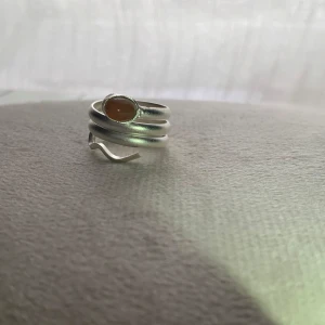 Silverfärgad ring med orange sten - Elegant silverfärgad ring med en vacker orange sten. Ringen har en unik design med flera lager som ger ett modernt och stilrent intryck. Perfekt för att ge en färgklick till din outfit.
