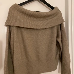 Beige offshoulder tröja - Säljer en mysig beige offshoulder tröja med ribbad kant. Perfekt för kyliga dagar med sin mjuka och bekväma passform. Tröjan har långa ärmar och en bred krage som ger en stilren look.