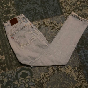 Ljusa jeans från Levi's - Säljer ett par ljusa Levi's jeans med klassisk femficksdesign och knappgylf. De har en straight passform och är perfekta för en avslappnad stil. 