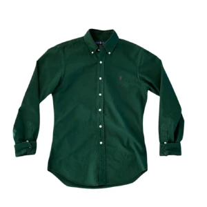 Grön långärmad skjorta från Ralph Lauren - Snygg grön långärmad skjorta från Ralph Lauren med klassisk krage och knappar framtill. Perfekt för en stilren look. Den har en liten broderad logga på bröstet som ger en extra touch av elegans. Helt ny!