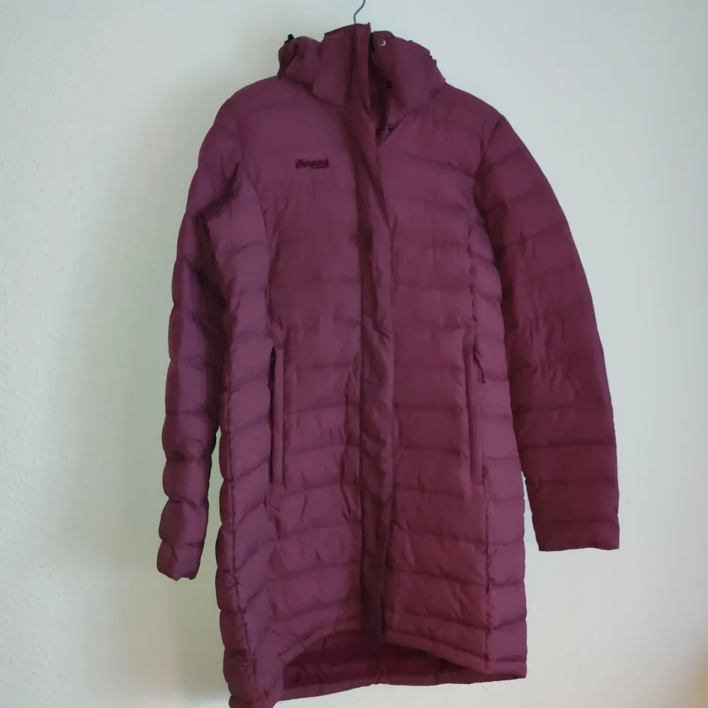Säljer en vinröd dunjacka från Bergans. Jackan har en lång design med dragkedja och huva, perfekt för kyliga dagar. Den quiltade stilen ger extra värme och komfort. Ett måste för vintern! ❄️. Takit.