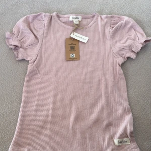 Ribbad topp i rosa och vit från Newbie - Säljer två söta ribbade toppar från Newbie i rosa och vit. De har puffiga kortärmar och en mjuk, bekväm passform. Perfekta för en avslappnad stil.