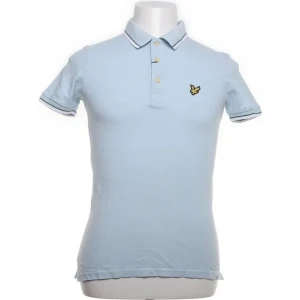 Ljusblå pikétröja från Lyle & Scott - Säljer en stilren ljusblå pikétröja från Lyle & Scott med korta ärmar och klassisk krage. Tröjan har en broderad logotyp på bröstet och knappar framtill. Perfekt för en avslappnad look.