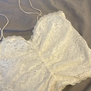 Vit spetslinne från BikBok - Säljer ett vackert vitt spetslinne från BikBok med tunna axelband. Linnet har ett blommigt mönster och är perfekt för en somrig look. Det är tillverkat i ett mjukt och bekvämt material som ger en romantisk känsla.