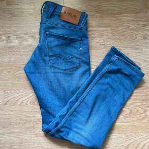 Blå jeans från Replay - Snygga blå jeans från Replay med klassisk femficksdesign och en läderpatch med logga på baksidan. De har en modern passform och är perfekta för en stilren look. Dragkedja och knapp framtill. Skriv om ni har funderingar! Priset är inte hugget i sten!
