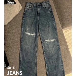 Blå jeans med slitningar - Snygga blå jeans i storlek S med slitningar på knäna för en trendig look. De har en klassisk femficksdesign och är perfekta för en avslappnad stil. Jeansen har en rak passform och fransiga benslut.