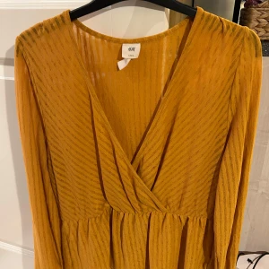 Gul omlott tröja från H&M - Snygg gul omlott tröja från H&M med v-ringning och långa ärmar. Tröjan har ett subtilt randigt mönster och är perfekt för  vardag.Den är tillverkad i ett lätt och luftigt material.