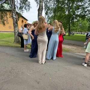 Champagnefärgad långklänning - Elegant champagnefärgad långklänning i satin med smala axelband och v-ringad design. Köpt från bohoo för 600 kronor. Använd en gång på min bal. Den är omsydd av sömmerska där fram som man ser på bilden. 